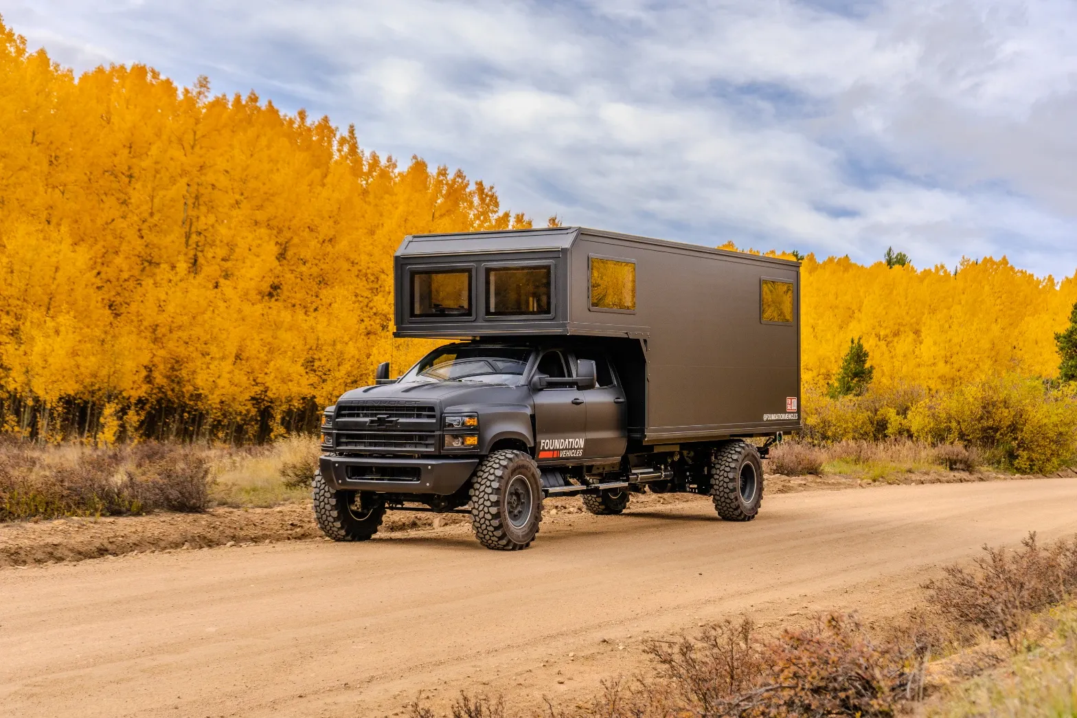 Chevrolet 6500 expedition camper on a mountain dirt road with golden aspens behind