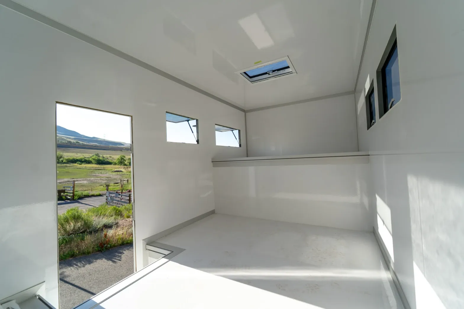 Interior of an empty white composite body with an open entry door onto a field