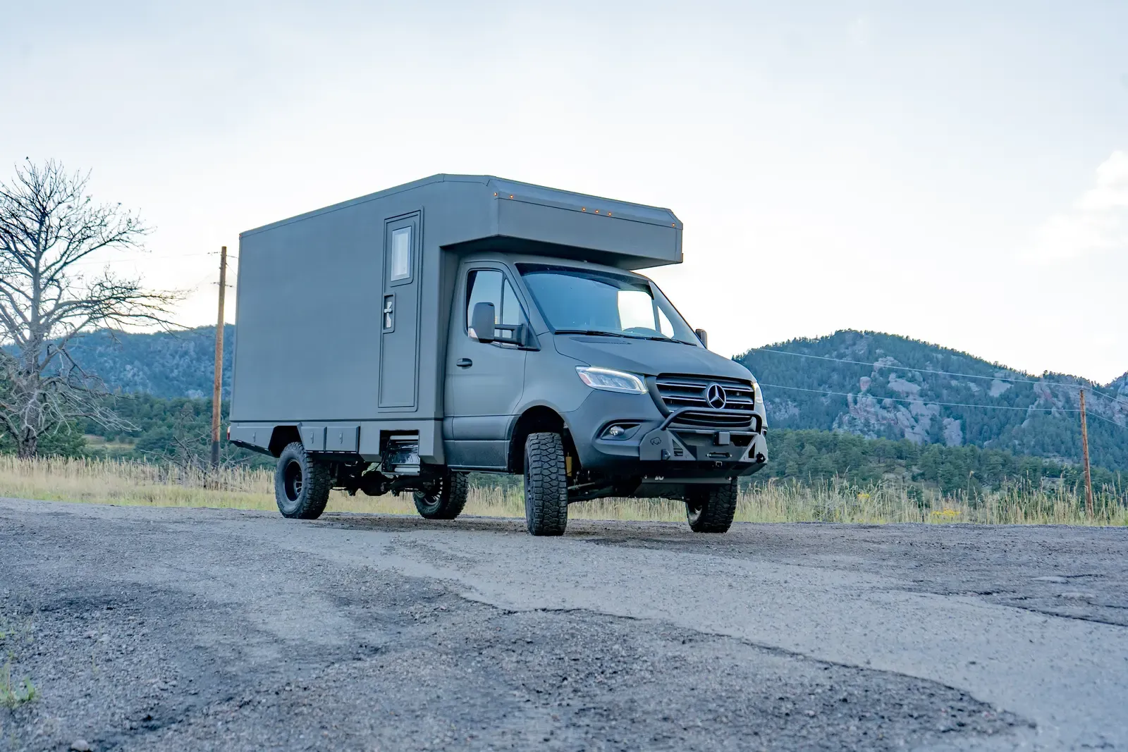 Matte-olive FV-170 demo composite box camper on an AWD Mercedes-Benz Sprinter 170, front three-quarter view at dusk with the Colorado foothills behind