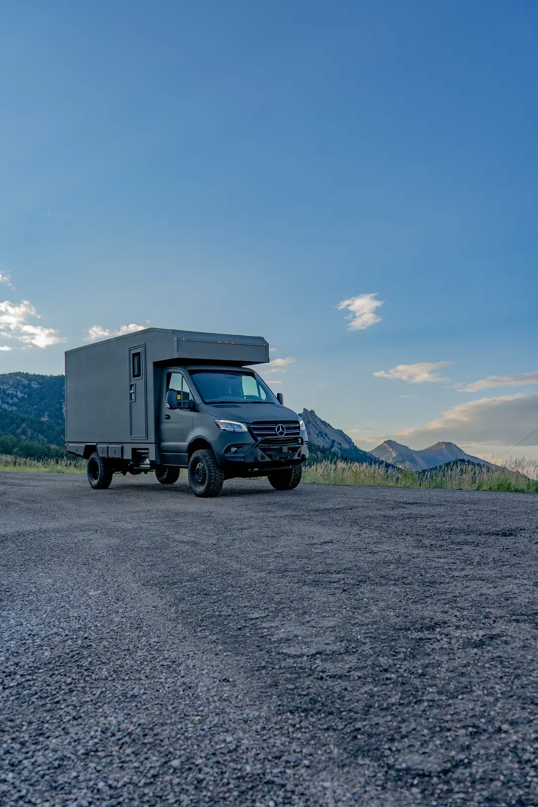 Matte-olive FV-170 demo composite camper on a Mercedes-Benz Sprinter 170 driving away on a gravel road at dusk