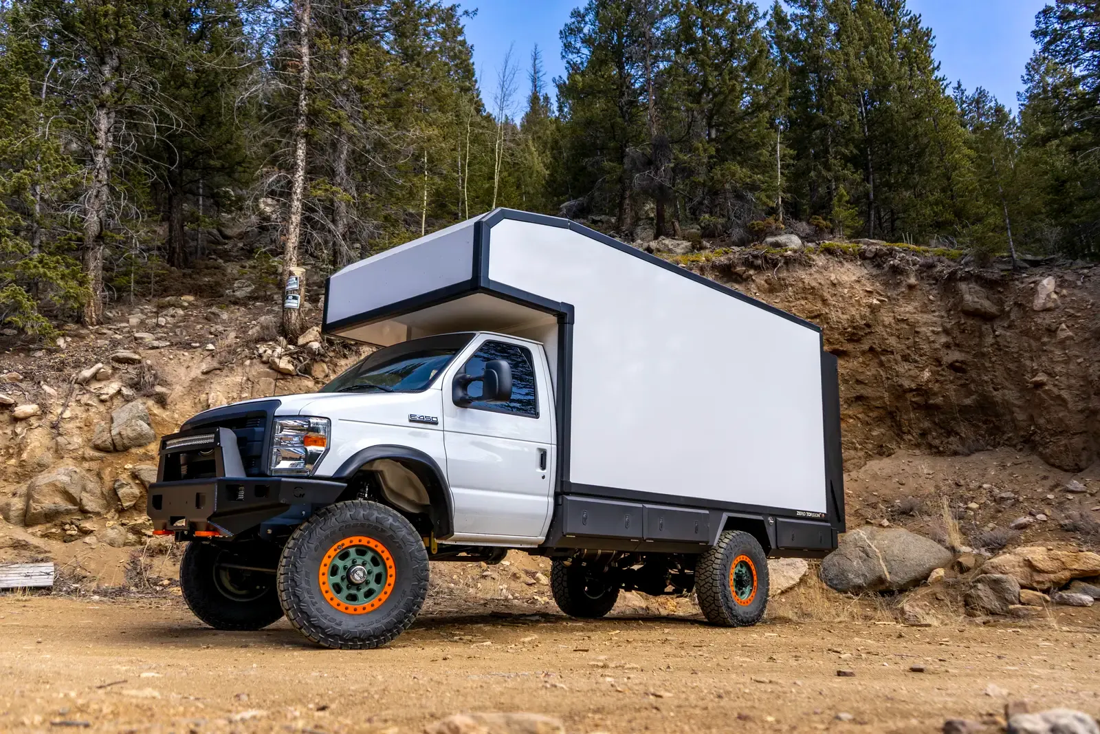 White E-158 composite box camper on a Ford E-Series 4x4, front three-quarter view on a rocky mountain trail