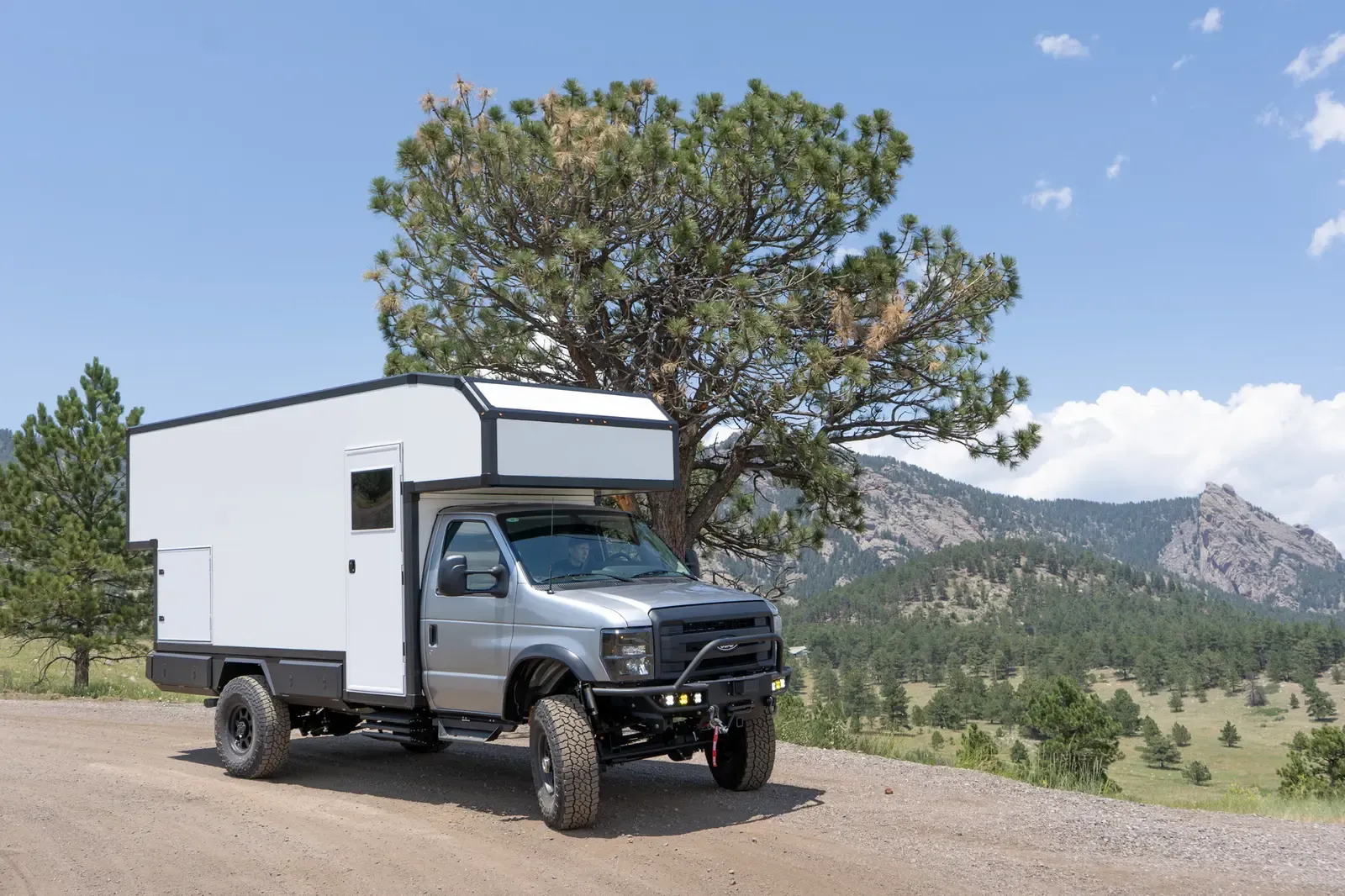 Ford E-450 4x4 with a dark cab and a white Foundation composite expedition body, side profile on a dirt road below the foothills