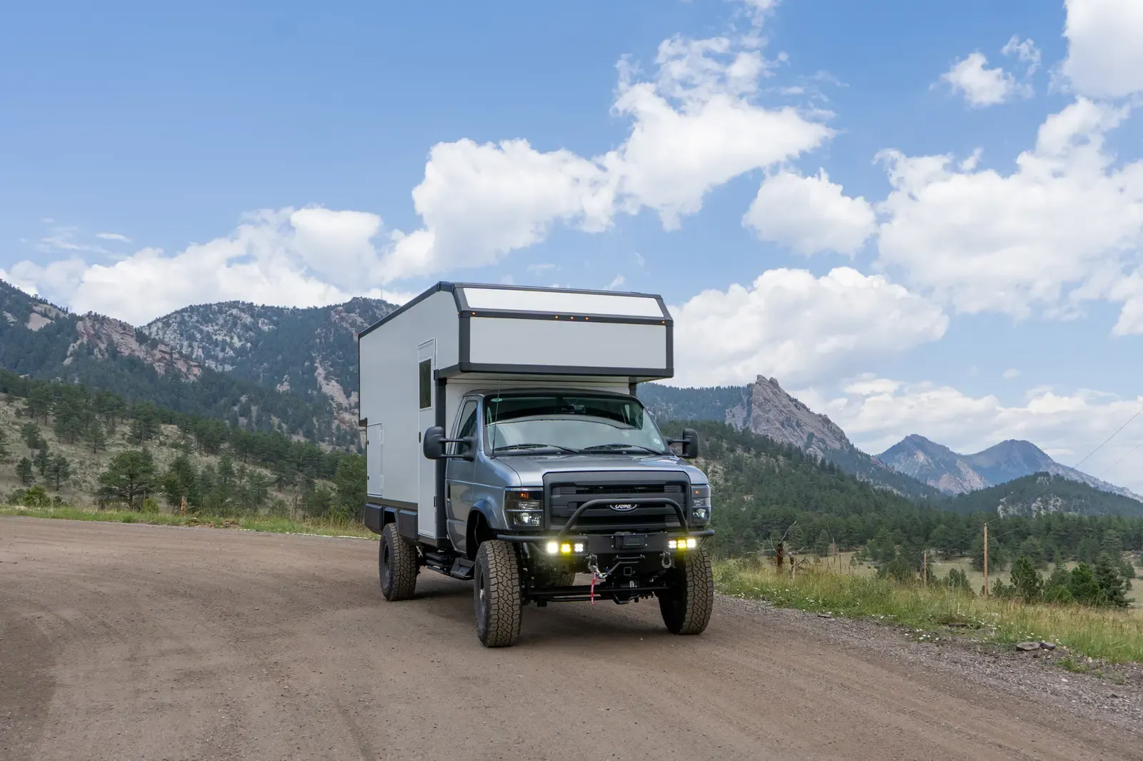 Ford E-450 4x4 custom expedition camper on 37-inch tires and super singles, driving a dirt road with its headlights on
