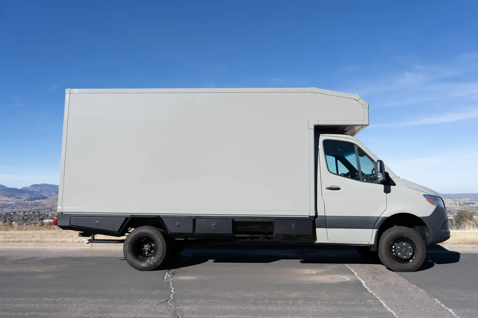White commercial box body on a Mercedes-Benz Sprinter cab-chassis, side profile with the foothills behind