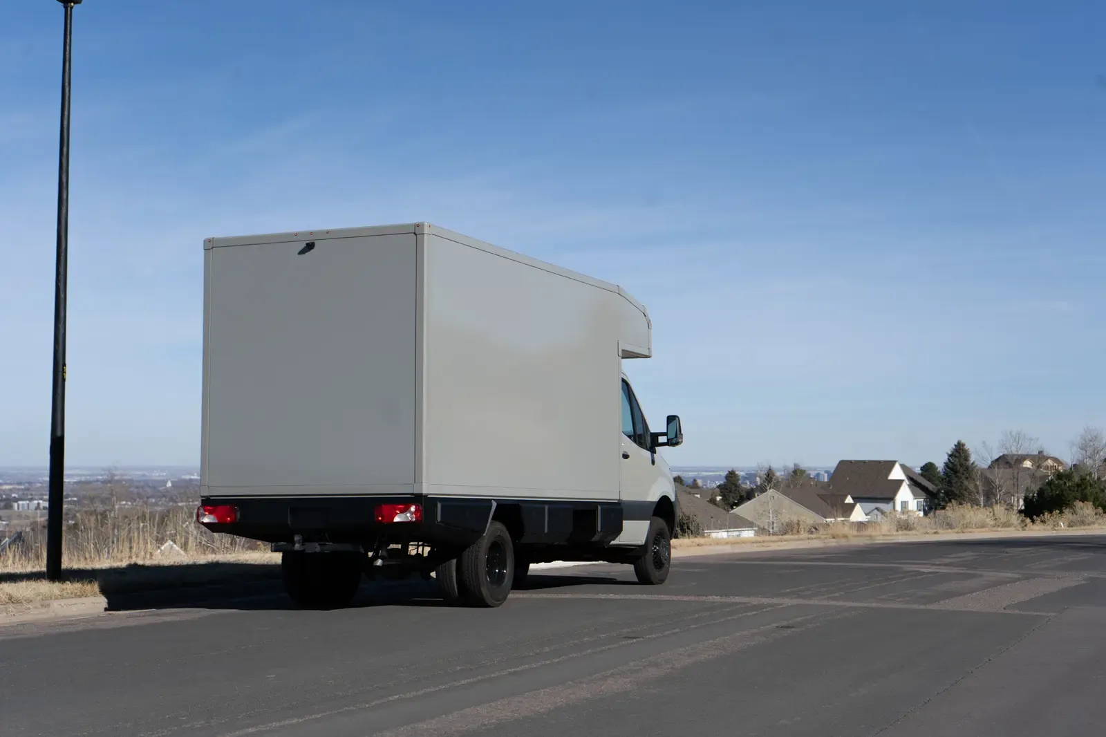 White commercial box body on a Mercedes-Benz Sprinter cab-chassis driving away on a country road