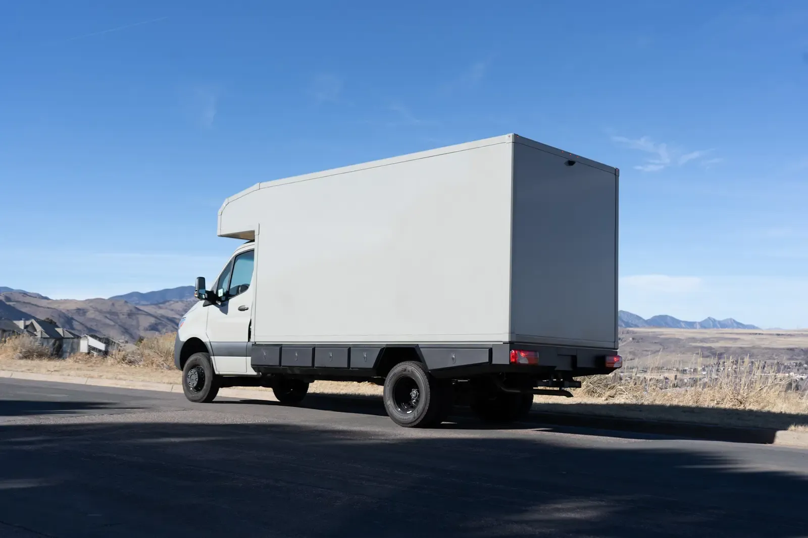 White commercial box body on a Mercedes-Benz Sprinter cab-chassis on a road with the foothills behind