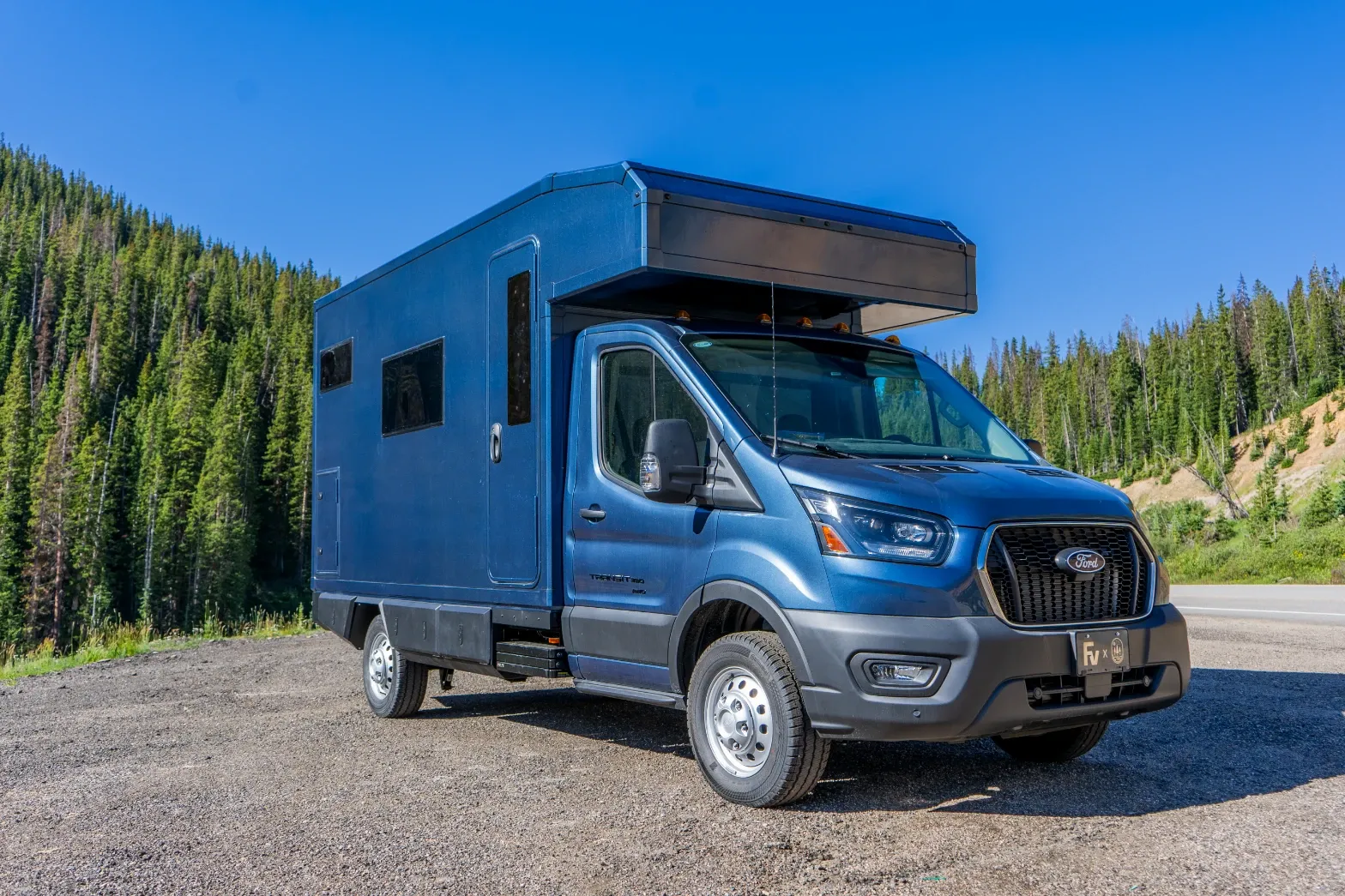 Blue composite camper on a Ford Transit AWD chassis, parked on a forest road in the Colorado high country