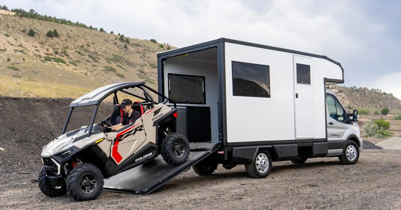 A side-by-side ATV driving up the lowered rear ramp of a Foundation Vehicles RampDeck body on a Ford Transit 156