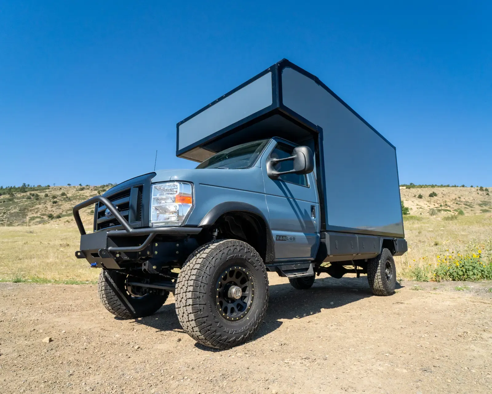 Two-tone composite box camper on a Ford E-Series 4x4, front three-quarter view under a blue sky