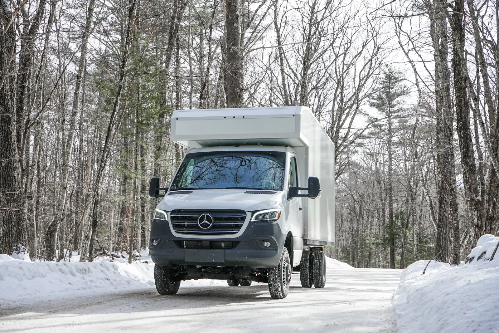 White composite box camper on a Mercedes-Benz Sprinter 170 on a snow-lined forest road, front three-quarter view